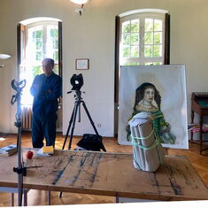 Fotograf Boris Becker steht im Museum in Schloss Wiepersdorf. Neben ihm ist ein Gemälde und eine Kamera zu sehen, vor ihm ein Tisch.