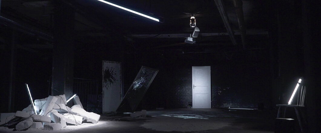 A dark exhibition space with a white door, white stones or rubble, and white fluorescent lights.