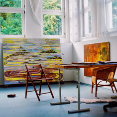 EIn Künstleratelier mit großformatigen Gemälden, davor Stühle und ein Tisch