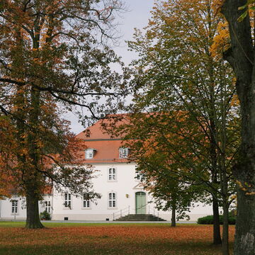 View of the front of Wiepersdorf Castle with trees in the foreground and leaves on the lawn
