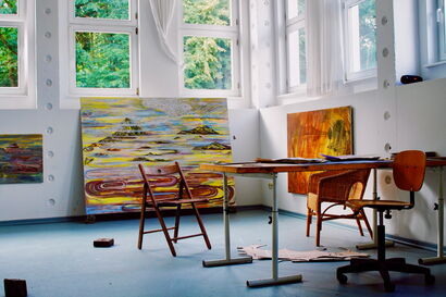 An artist's studio with large-scale paintings, with chairs and a table in front of it