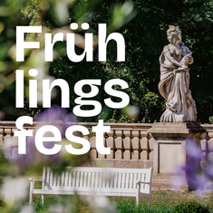 View of the park at Wiepersdorf Castle with a sculpture in the background and a white park bench in the foreground. "Spring Festival" is written on top of it.