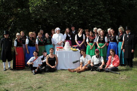 All the actors and actresses from the short film and the crew are lined up in front of a table with a cake