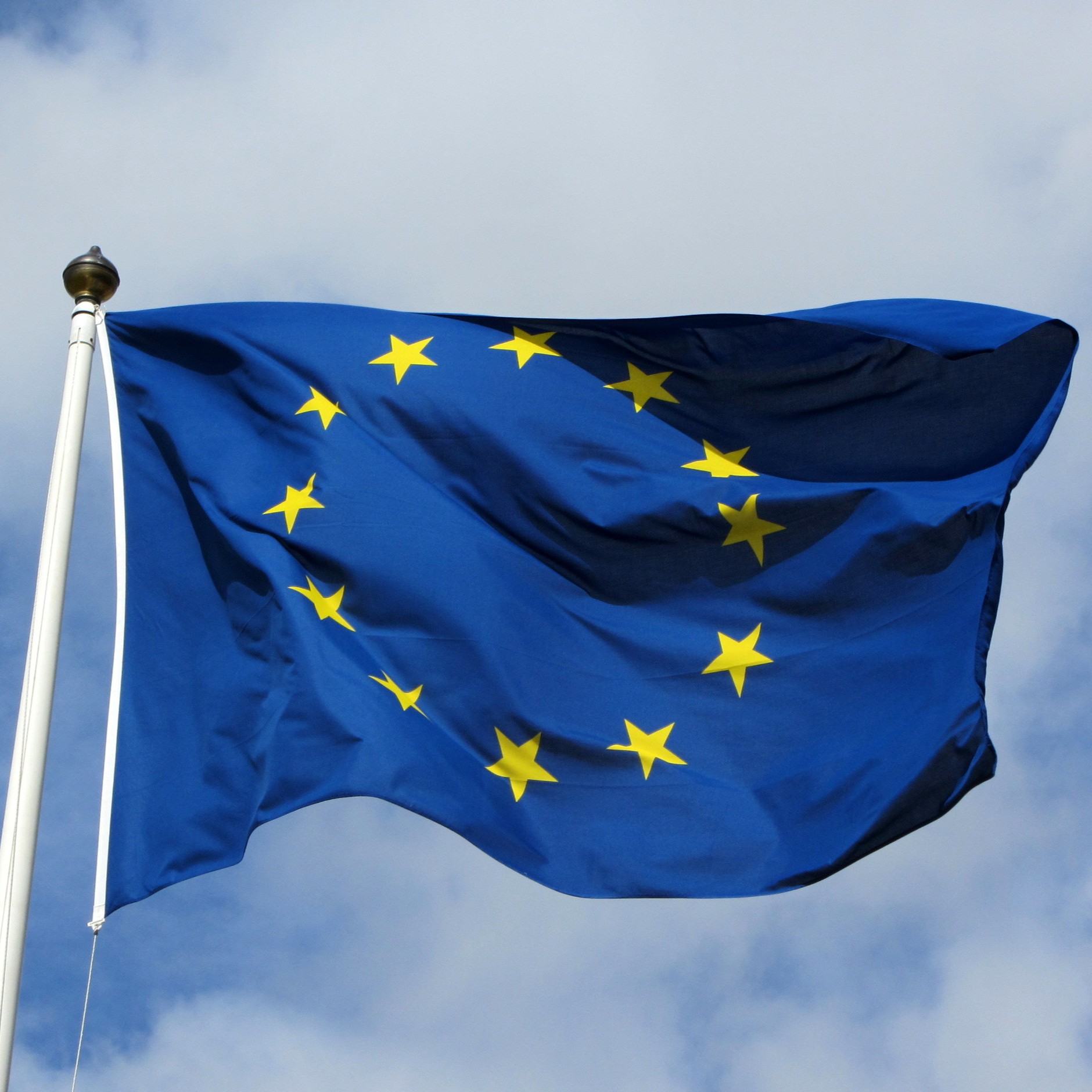 The EU flag flutters in the wind, with a blue sky behind it